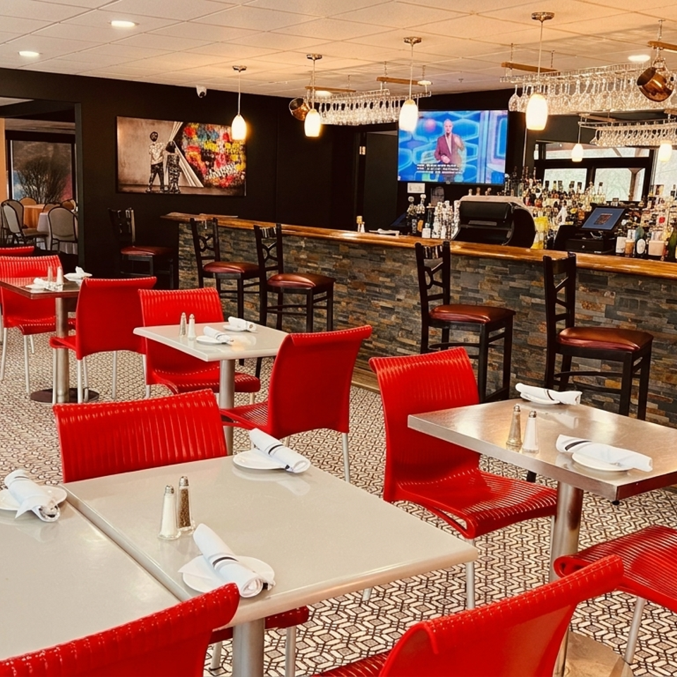 Stylish restaurant dining room with red chairs, set tables, patterned flooring, and a fully stocked bar beneath pendant lights.