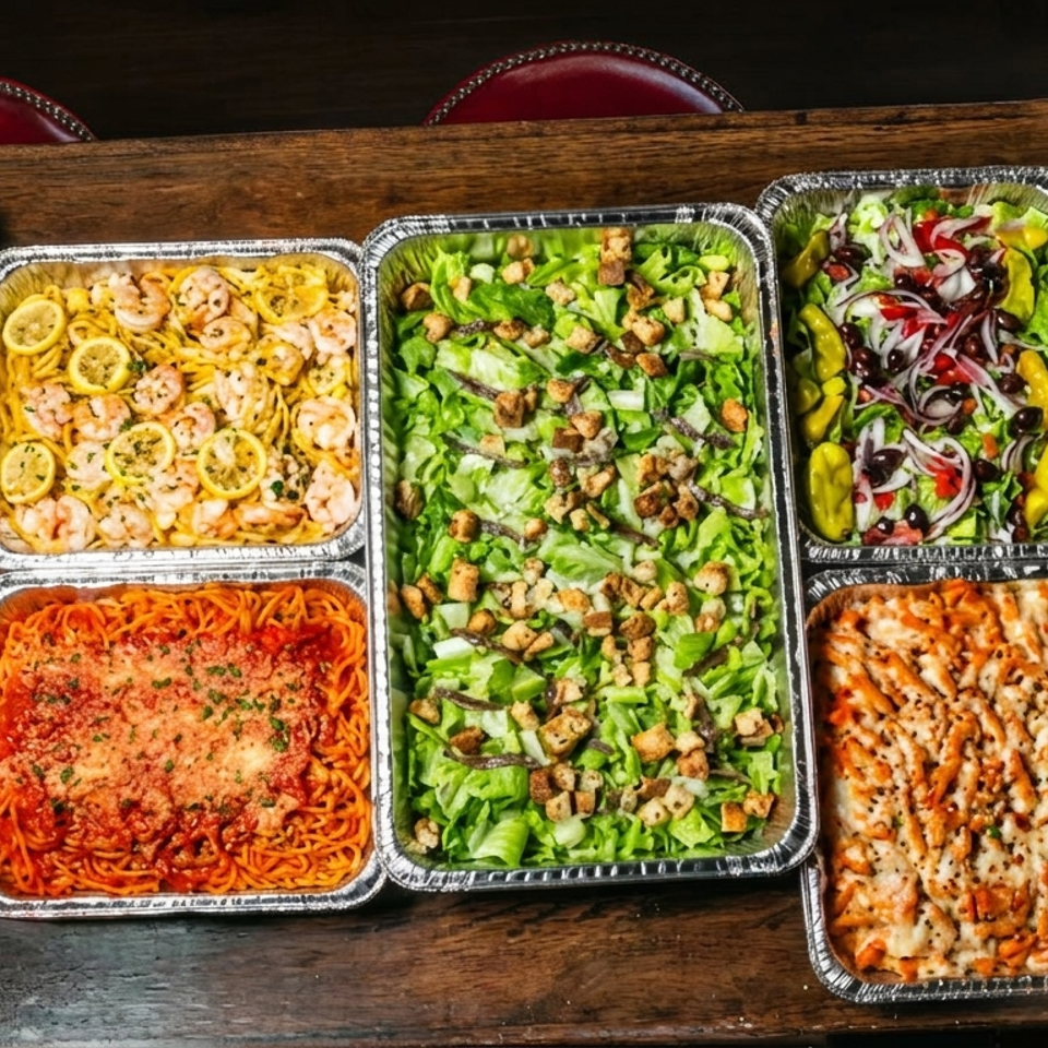Aluminum trays display broccoli, shrimp pasta, salads, garlic bread, spaghetti, ravioli, baked pasta, and meatballs on a wooden table.